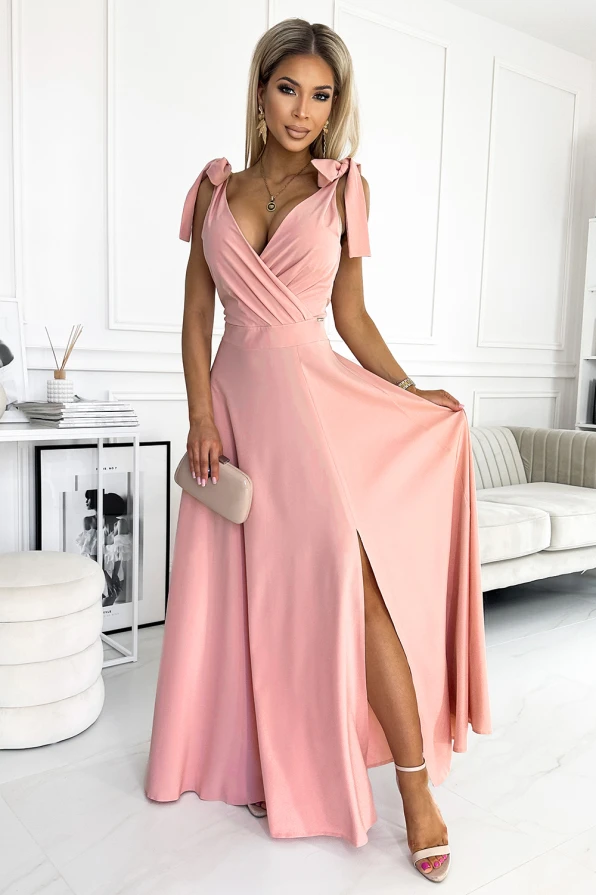 Eine elegante, lange Abendkleid in zartem Rosa mit tiefem V-Ausschnitt und Schleifendetails an den Schultern. Der fließende Stoff und der hohe Beinschlitz verleihen dem Kleid eine feminine und stilvolle Note.