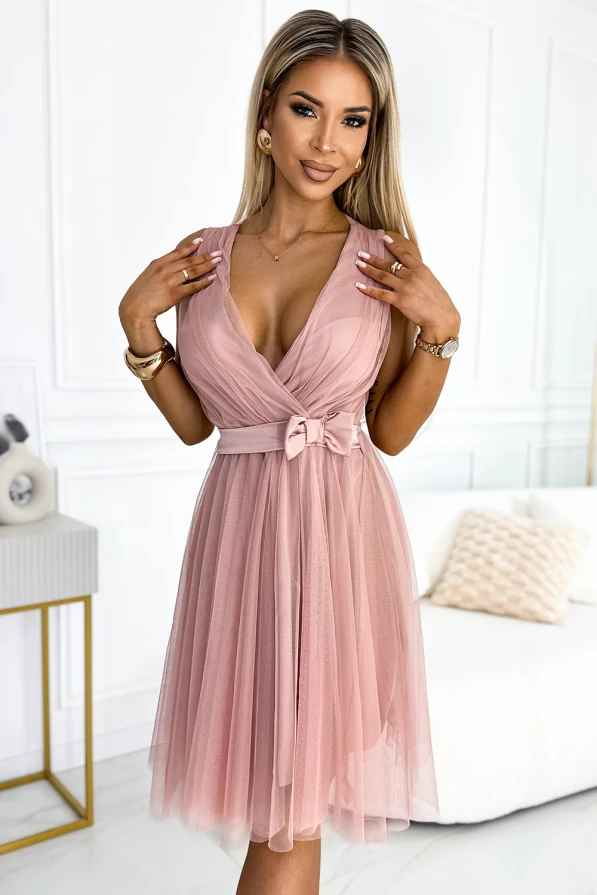 Elegantes, ärmelloses Kleid aus zartem Tüll in einem sanften Rosaton, mit einem tiefen V-Ausschnitt und einer dekorativen Schleife in der Taille. Perfekt für besondere Anlässe, kombiniert es feminine Eleganz mit einem modernen Schnitt.