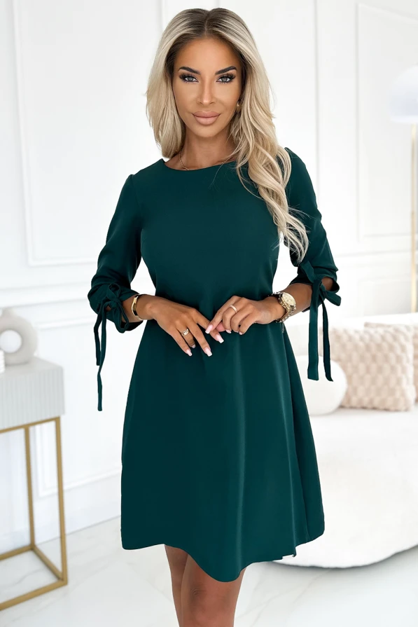 Elegantes, trapezförmiges Kleid in tiefem Grün mit langen Ärmeln und dekorativen Schleifen. Perfekt für formelle Anlässe oder stilvolle Abendveranstaltungen.