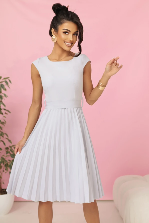 Modelka w eleganckiej plisowanej sukience midi marki Numoco w kolorze jasnoszarym, z krótkim rękawkiem i wiązaniem w talii, prezentująca kreację idealną na wesele, komunię i inne uroczystości.