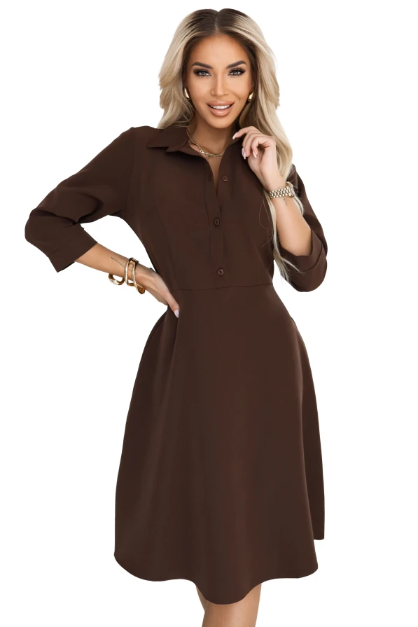 Modelka prezentuje klasyczną szmizjerkę w kolorze czekoladowym, podkreślając jej elegancki fason, wiązanie w talii i uniwersalny charakter.