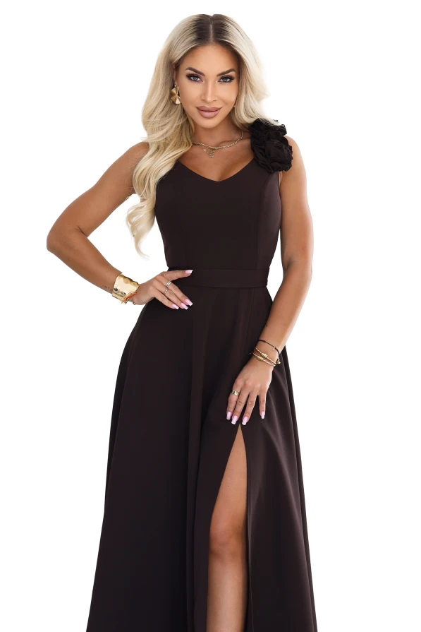 Das Model trägt ein elegantes schokoladenbraunes Maxikleid mit herzförmigem Ausschnitt, Beinschlitz und einer dekorativen Blume an der Schulter.