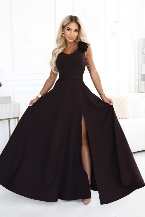 Das Model trägt ein elegantes schokoladenbraunes Maxikleid mit herzförmigem Ausschnitt, Beinschlitz und einer dekorativen Blume an der Schulter.