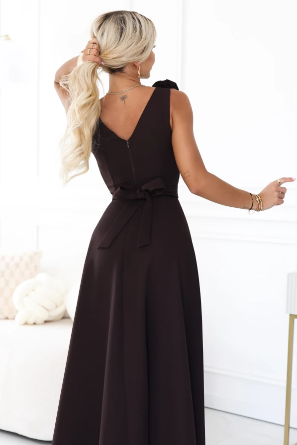 Das Model trägt ein elegantes schokoladenbraunes Maxikleid mit herzförmigem Ausschnitt, Beinschlitz und einer dekorativen Blume an der Schulter.