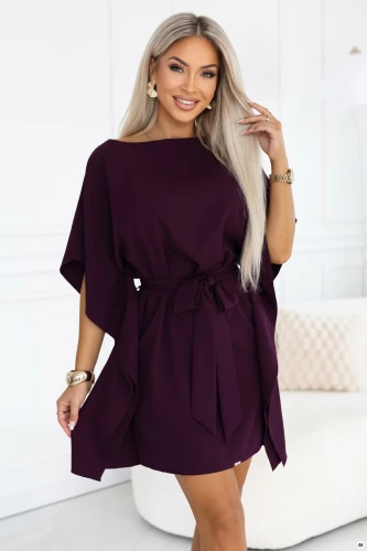 Model im Kimonokleid von Numoco in reifer Pflaume mit Bootausschnitt, weiten Ärmeln, in der Taille gebundenem Gürtel und drapierten Seiten, knapp über dem Knie.}