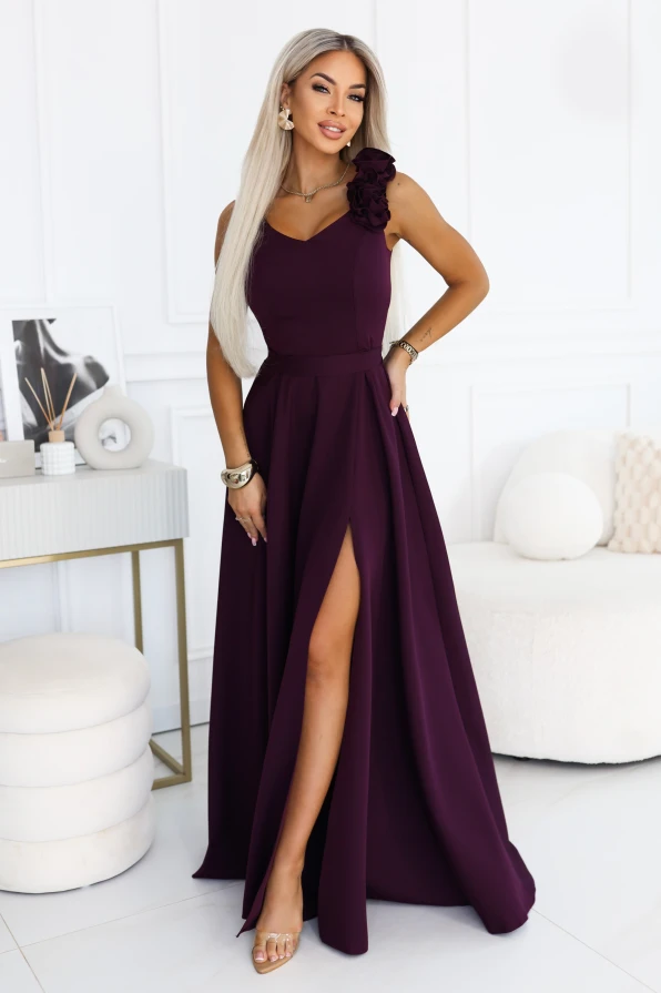 Model im Maxikleid von Numoco in reifer Pflaume mit V-Ausschnitt, dekorativen Rosen an der Schulter, betonter Taille und ausgestelltem Rockteil mit hohem Beinschlitz.