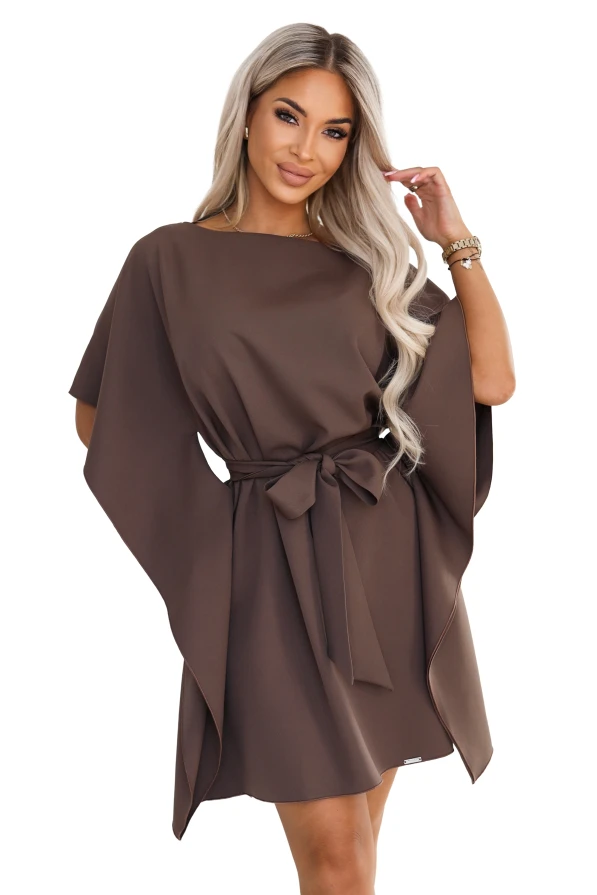 Model im Kleid SOFIA von Numoco in einem Mokkabraun-Ton. Das Kleid reicht knapp über das Knie, hat einen Bootausschnitt, weite Schmetterlingsärmel und einen in der Taille zur Schleife gebundenen Gürtel.