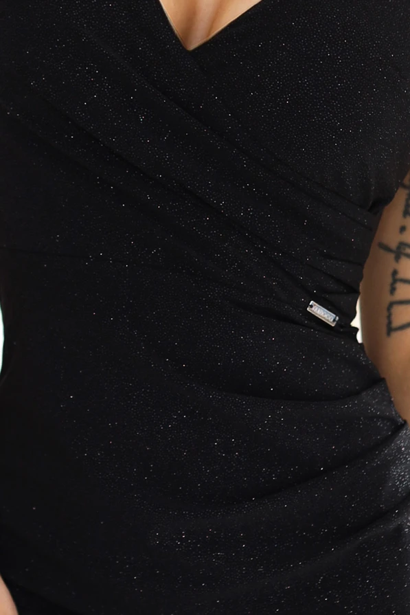 Modelka prezentuje elegancką, dopasowaną sukienkę koktajlową marki Numoco w kolorze czarnym z subtelnym brokatowym połyskiem. Stylizacja idealna na wieczorne wyjście, wykonana w Polsce – kobiecy fason z kopertowym dekoltem i cienkimi ramiączkami podkreśla sylwetkę.