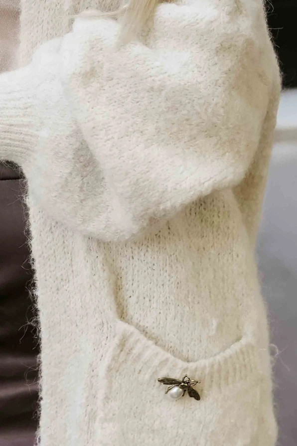 Modelka w stylowym beżowym kardiganie z miękkiej dzianiny, z ozdobną broszką i kieszeniami, w eleganckiej stylizacji miejskiej – Numoco Basic.