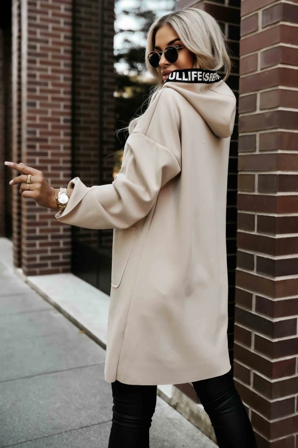 Modelka prezentuje beżowy płaszczyk damski z kapturem i ozdobnymi taśmami „LIFE IS BEAUTIFUL” marki Numoco Basic.