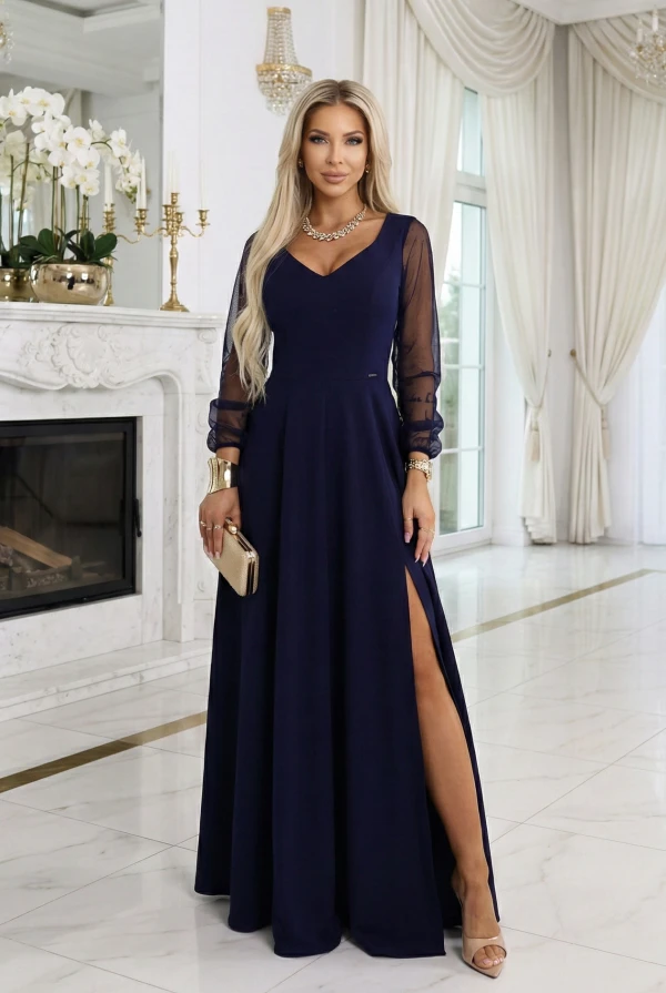 Modelka w eleganckiej, granatowej sukni maxi z dekoltem V, transparentnymi długimi rękawami i rozcięciem na nodze, prezentująca wieczorową stylizację na wesele, galę lub przyjęcie w jasnym, minimalistycznym wnętrzu.
