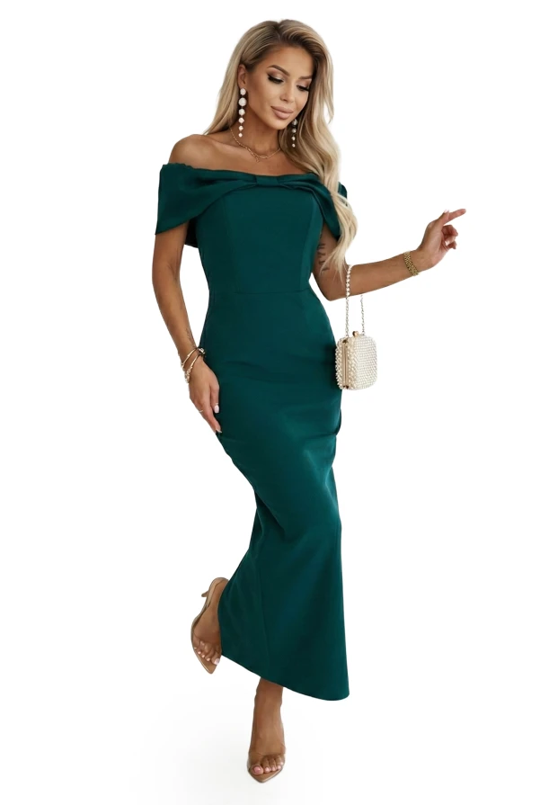 Wieczorowa sukienka maxi w odcieniu butelkowej zieleni z kokardą na dekolcie, pokazana na modelce w eleganckiej aranżacji.