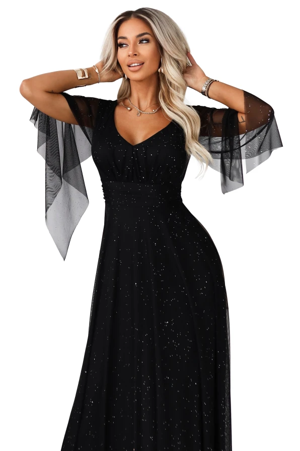 Czarna sukienka maxi o kroju empire, z ozdobnymi rękawami i błyszczącymi akcentami, prezentowana na tle białego, eleganckiego wnętrza.